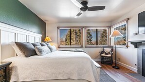 Une chambre à coucher comprenant un lit, une table de chevet, une lampe, une chaise, une cheminée et une fenêtre avec des stores.