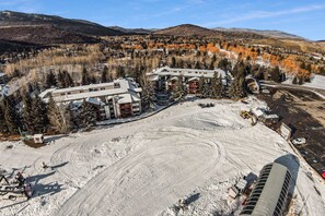 A snow-covered landscape with a building complex, including a hotel with multiple floors and a ski lift.
