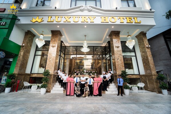 A luxury hotel entrance with a grand facade, large columns, and a group of staff members standing in front.