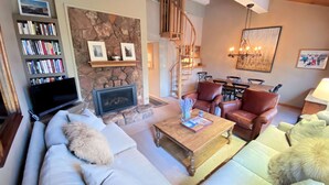 A cozy living room with a fireplace, a bookshelf, leather chairs, and a dining area.