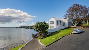 A modern house with a view of a lake, a paved driveway, and a white car parked on the street.