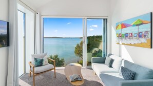 A modern living room with a large sliding glass door leading to a balcony overlooking a body of water.