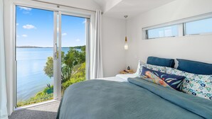 A bedroom with a large bed, a view of the sea, and a window with curtains.