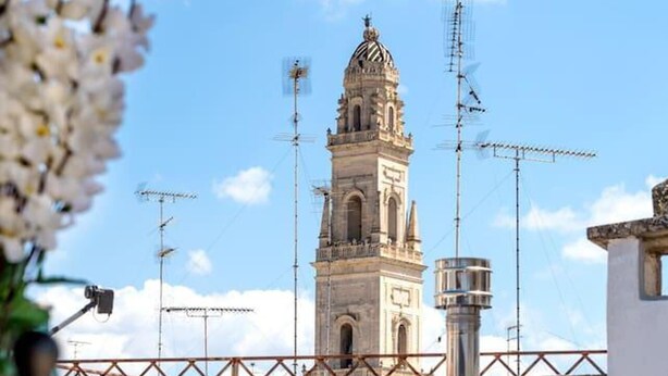 A terrace with a view of a historic tower and antennas, a table with a chair, and a vase of flowers. - Holiday Home Sleeps 6 in the Historic Center of Le (Lecce)