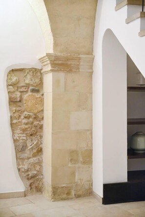 Un mur de pierre jouxtant un mur blanc, sur lequel se trouve une étagère portant un grand pot.
