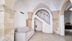 A spacious living area with a stone wall, a light-colored sofa, a staircase with a metal railing, and a tiled floor. - Holiday Home Sleeps 6 in the Historic Center of Le (Lecce)