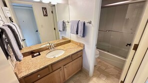 A bathroom with a granite countertop, two sinks, a mirror, and a glass shower enclosure.