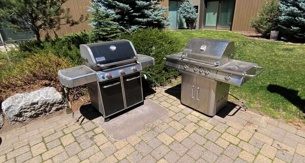 Two stainless steel barbecue grills with control knobs and a built-in thermometer, placed on a paved patio with a grassy area and trees in the background. - Vail Mountain Views From Upper Level 2BR Condo - In Unit Washer/Dryer (Vail)