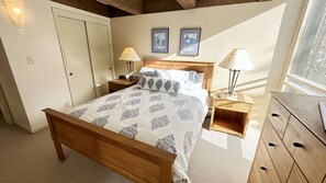 A bedroom with a wooden bed, two bedside tables with lamps, a wooden dresser, and two framed pictures on the wall.