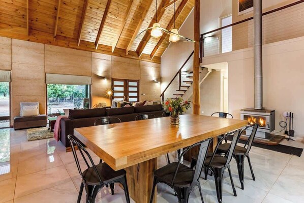 Amplia sala de estar con una mesa de comedor de madera, sillas negras, un sofá y una chimenea.