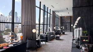 A modern hotel lobby with a large window, a seating area, and a buffet table. - Ascott Embassy Sathorn Bangkok (Bangkok)