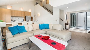 A modern living room with a beige sectional sofa, a white coffee table, and a staircase leading to an upper level. - Lakeview Retreat - Queenstown Holiday Home (Queenstown)
