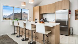 A modern kitchen with a central island, bar stools, a stainless steel refrigerator, and a window with a mountain view. - Lakeview Retreat - Queenstown Holiday Home (Queenstown)
