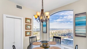 A dining area with a round table, chairs, a chandelier, and a large window offering a city view. - Beachfront With Spectacular Gulf Views-Private Balcony-Outdoor Pools-Fitness Center-Tennis Courts (Navarre)