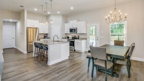 A spacious kitchen with a central island, white cabinetry, stainless steel appliances, and a dining area with a table and chairs. - Beautiful Pet Friendly Home With Private Pool - Minutes To Navarre Beach - Fast WiFi (Navarre)