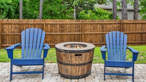 Two blue Adirondack chairs and a round wooden fire pit on a paved patio. - Beautiful Pet Friendly Home With Private Pool - Minutes To Navarre Beach - Fast WiFi (Navarre)