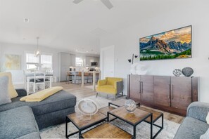 A modern living room with a grey sofa, yellow armchair, and a coffee table. There is a dining area with a white table and chairs, and a kitchen in the background. - Private Saltwater Pool (Heating Optional), With Excellent Ocean Views Only 2 Blocks From the Beach (Oak Island)