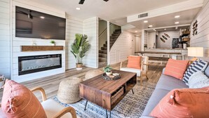 Una sala de estar moderna con chimenea, un televisor grande y una escalera que conduce a un nivel superior.