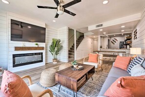 A modern living room with a fireplace, a large TV, and a staircase leading to an upper level. - Chic Fort Walton Condo ~ 2 Blocks to Beach! (Fort Walton Beach)