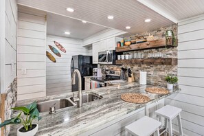 A modern kitchen with white cabinetry, a granite countertop, and a stone backsplash. - Chic Fort Walton Condo ~ 2 Blocks to Beach! (Fort Walton Beach)