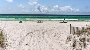 Una playa arenosa con una valla de madera, algunas personas y sombrillas.