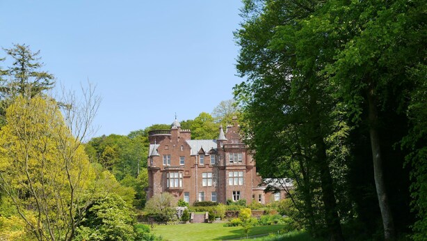 A large, historic building with multiple windows and a prominent tower, surrounded by lush greenery and a well-maintained lawn. - Croftdean -  a house that sleeps 6 guests  in 3 bedrooms (Dalbeattie)