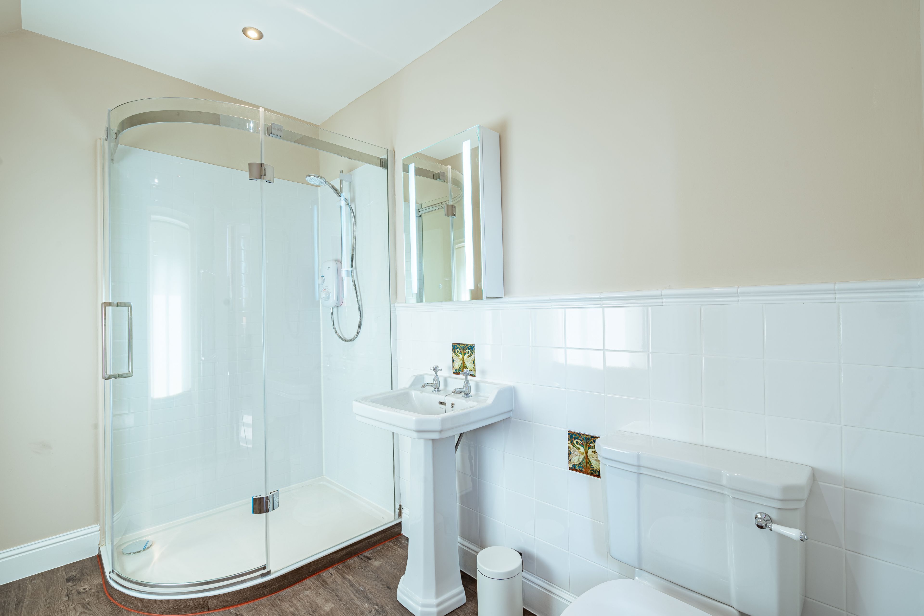 A bathroom with a glass shower enclosure, a pedestal sink, and a toilet.