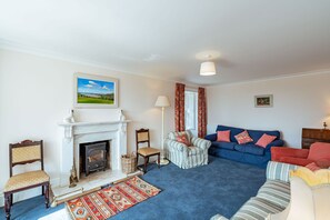A living room with a fireplace, a blue sofa, a striped armchair, and a red armchair.