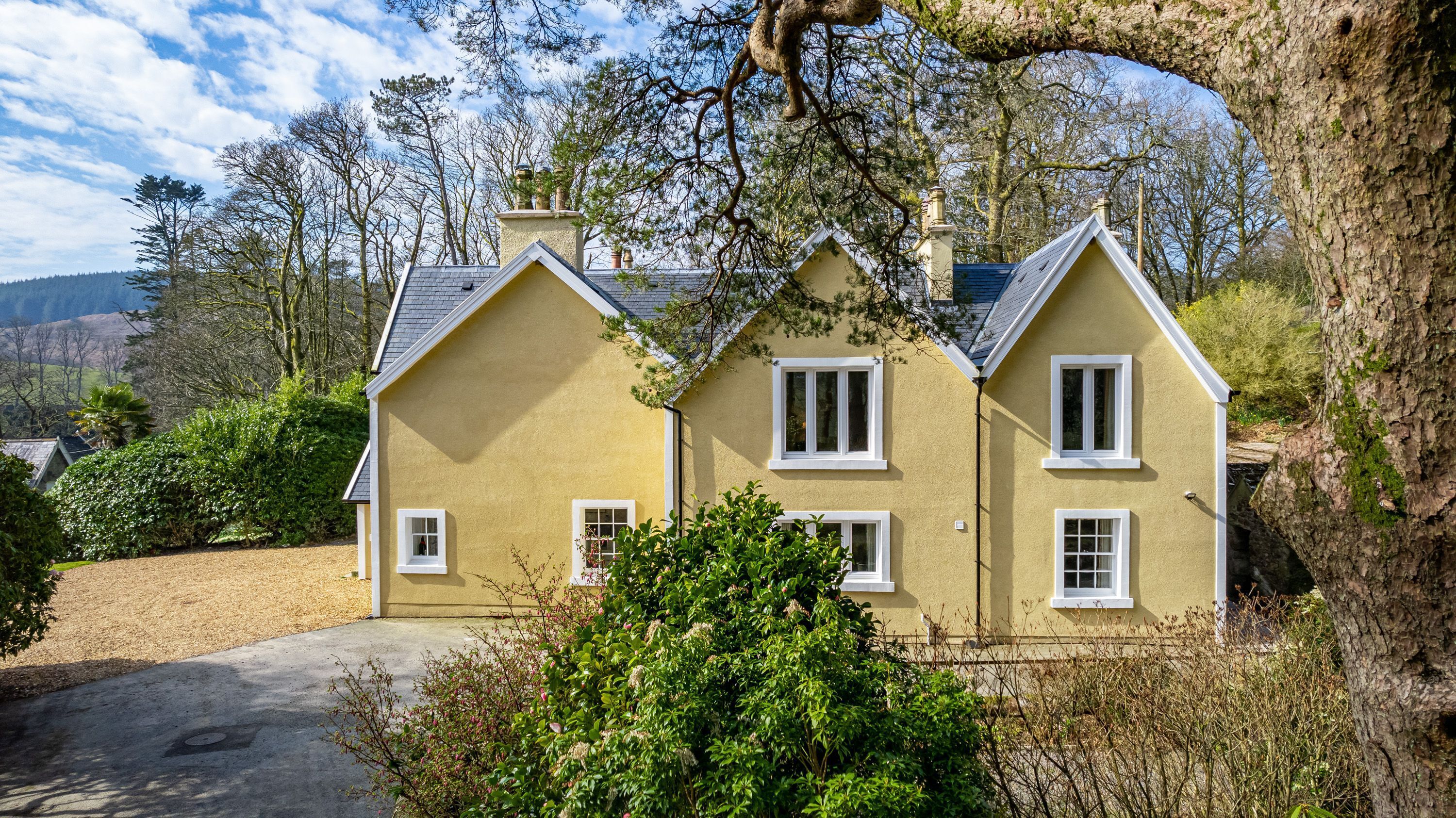 Ein zweistöckiges Haus mit gelber Fassade und weißem Zierrat, umgeben von Bäumen und einer Schotterauffahrt.