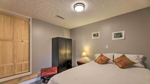 Une chambre à coucher avec un lit, une table de chevet, une lampe, une armoire et un fauteuil rouge.
