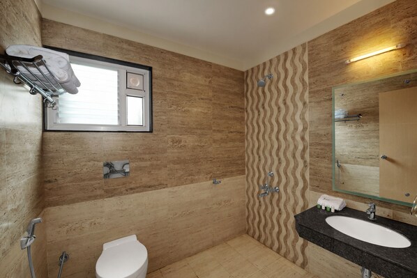 A modern bathroom with a marble wall, a shower, a toilet, a sink with a mirror, and a towel rack. - Jiwan Hotels (Rameshwaram)