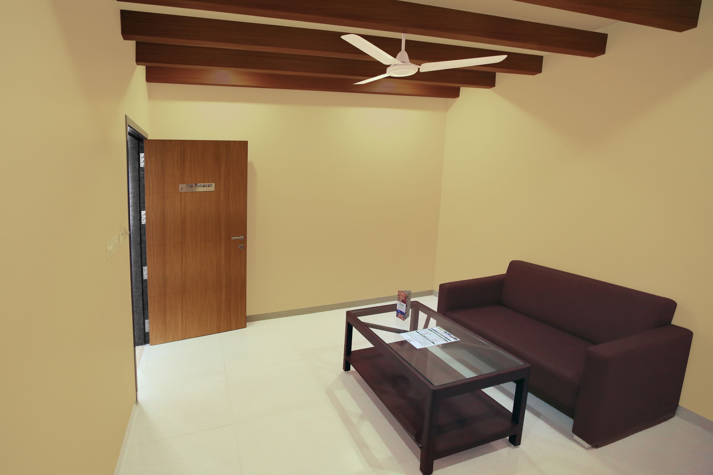 Una habitación con techo de madera, ventilador de techo, un sofá marrón y una mesa de centro con cubierta de vidrio.