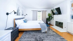 Een moderne slaapkamer met een bed, nachtkastjes, een televisie, een open haard en een raam met gordijnen.