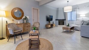 Ein modernes Wohnzimmer mit Sofa, Sessel, Couchtisch, Fernseher, Kamin und einem großen Spiegel.