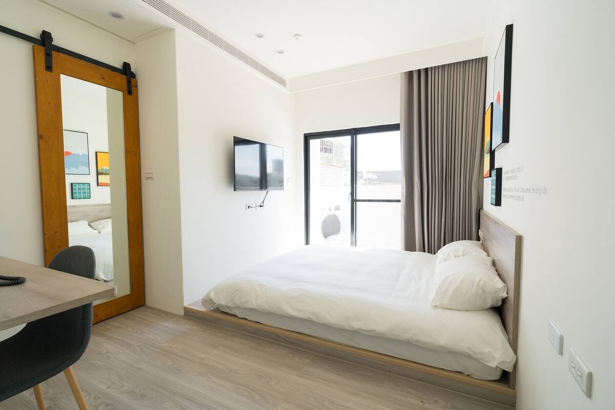 A modern hotel room with a bed, a desk, a chair, a TV, and a sliding door.