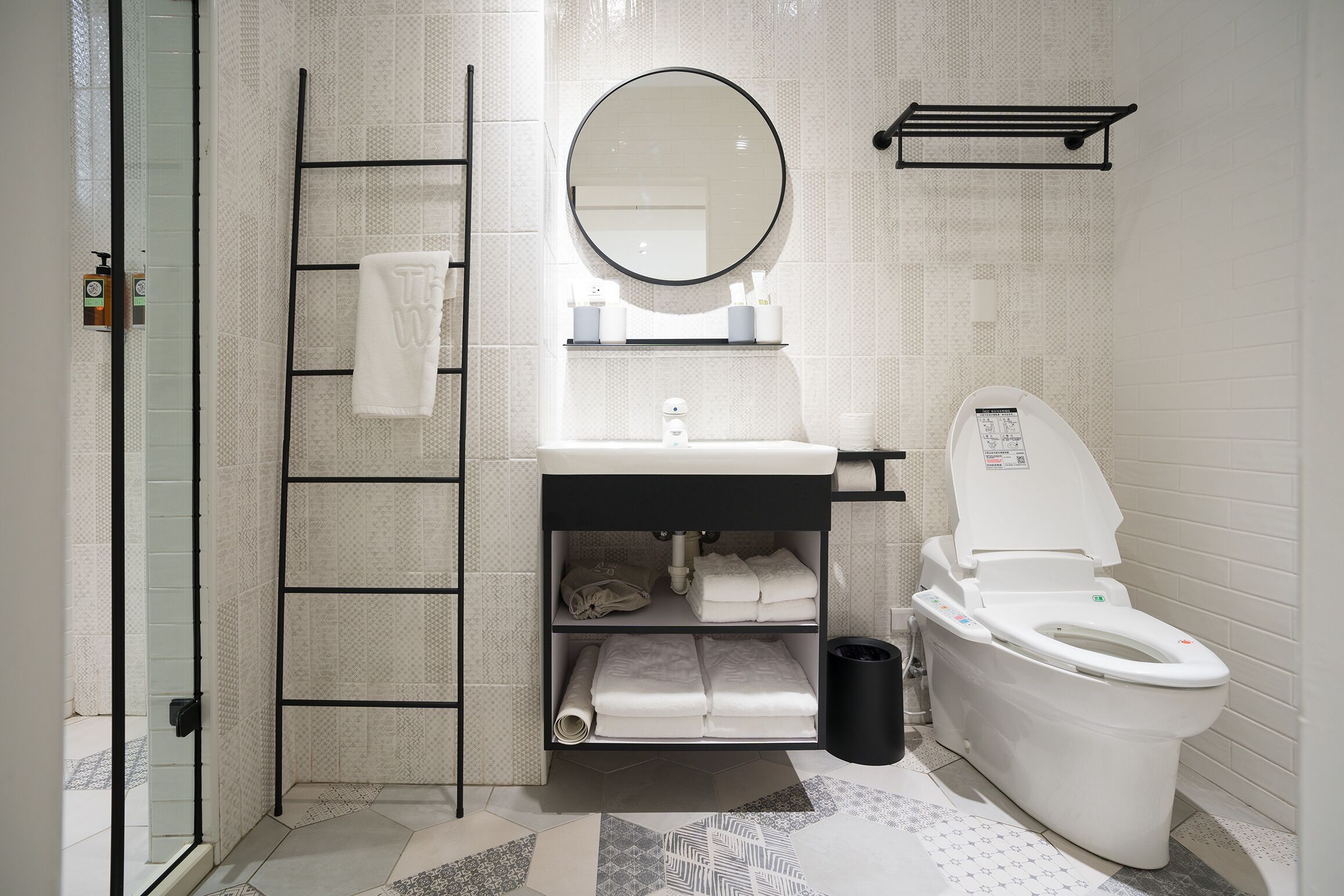 A modern bathroom with a white sink, a round mirror, a toilet, and a towel rack.