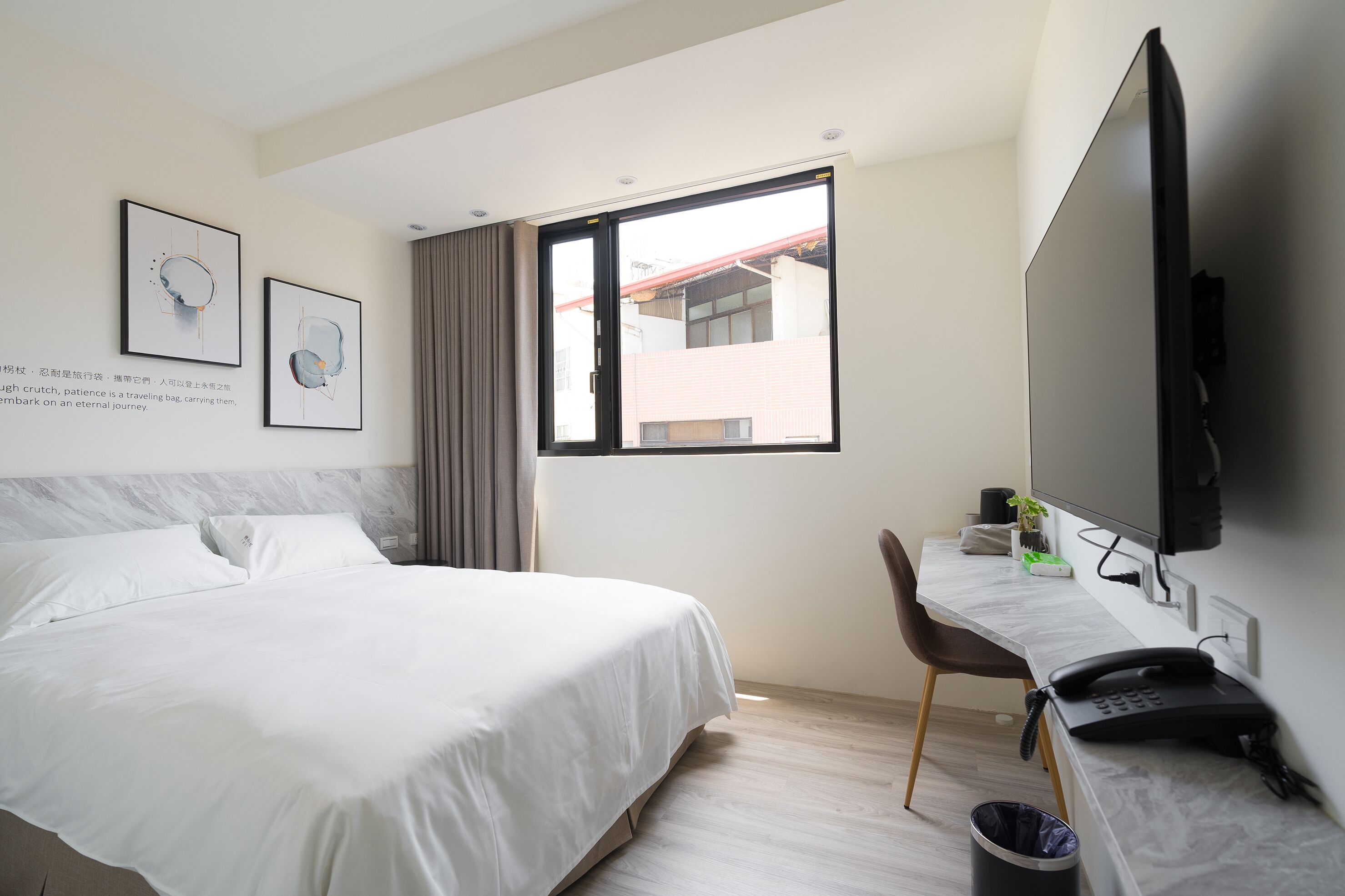 A hotel room with a bed, a desk, a television, and a window with a view of buildings.