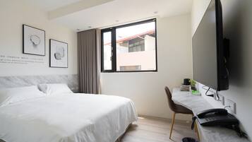 A hotel room with a bed, a desk, a television, and a window with a view of buildings.