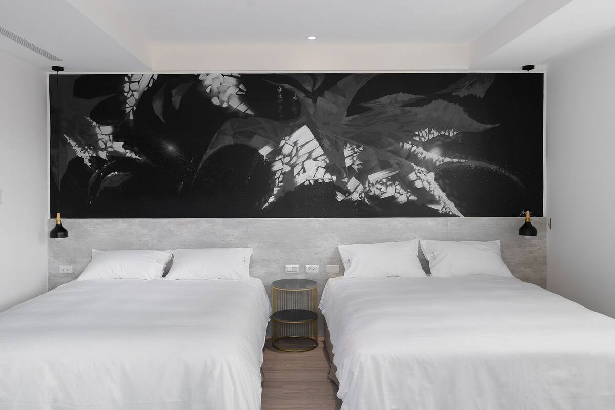 A modern bedroom with two beds, a large abstract artwork on the wall, and a small round table.