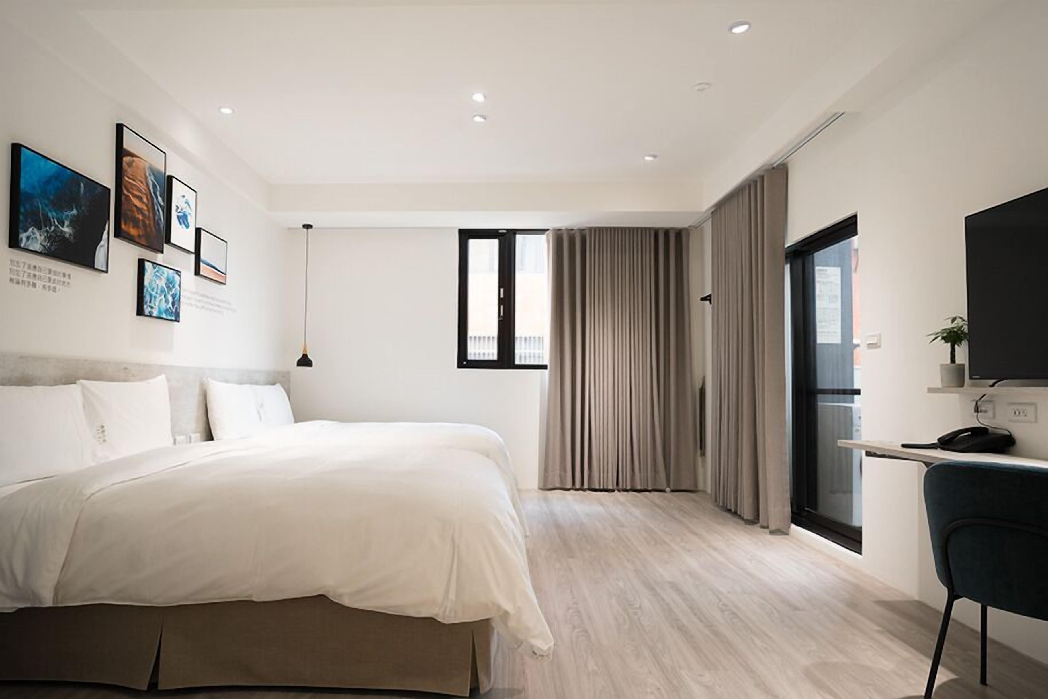 A modern bedroom with a large bed, a desk with a computer, and a TV.
