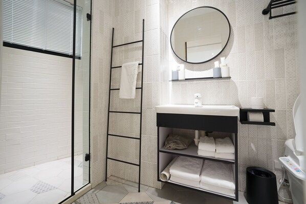 A modern bathroom with a glass shower enclosure, a black towel rack, a round mirror, and neatly arranged towels. - The Way Inn (Taichung)