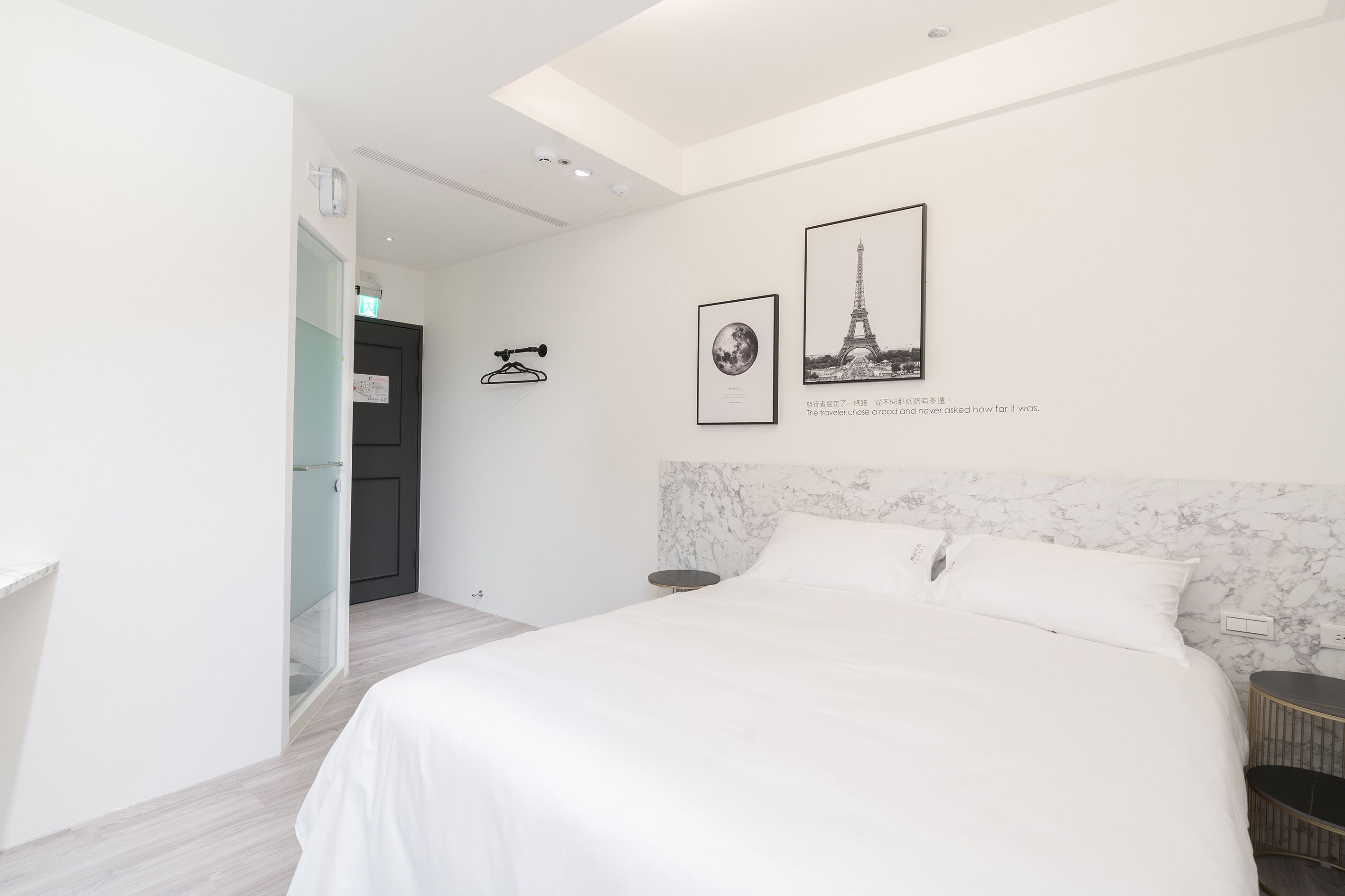 A modern hotel room with a large bed, a marble headboard, and two framed pictures on the wall.