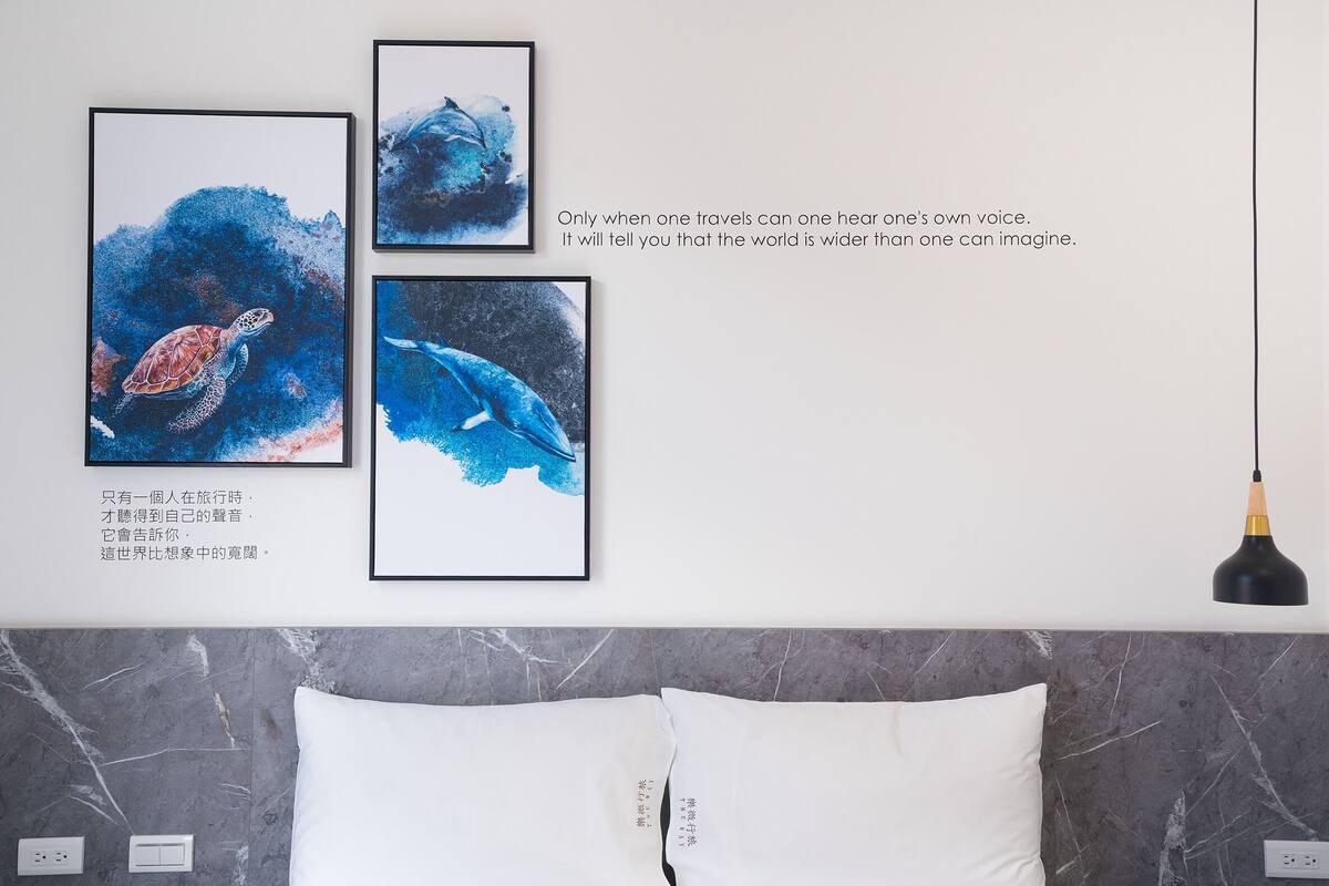 A bedroom with a marble headboard, a bed with white pillows, and three framed artworks depicting marine life.