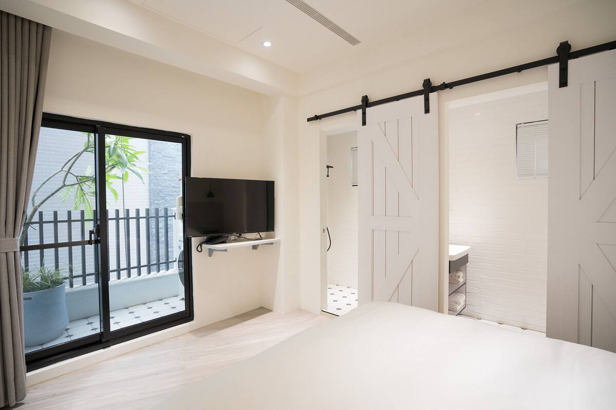 A bedroom with a sliding door to a balcony, a TV on a shelf, and a white wardrobe.