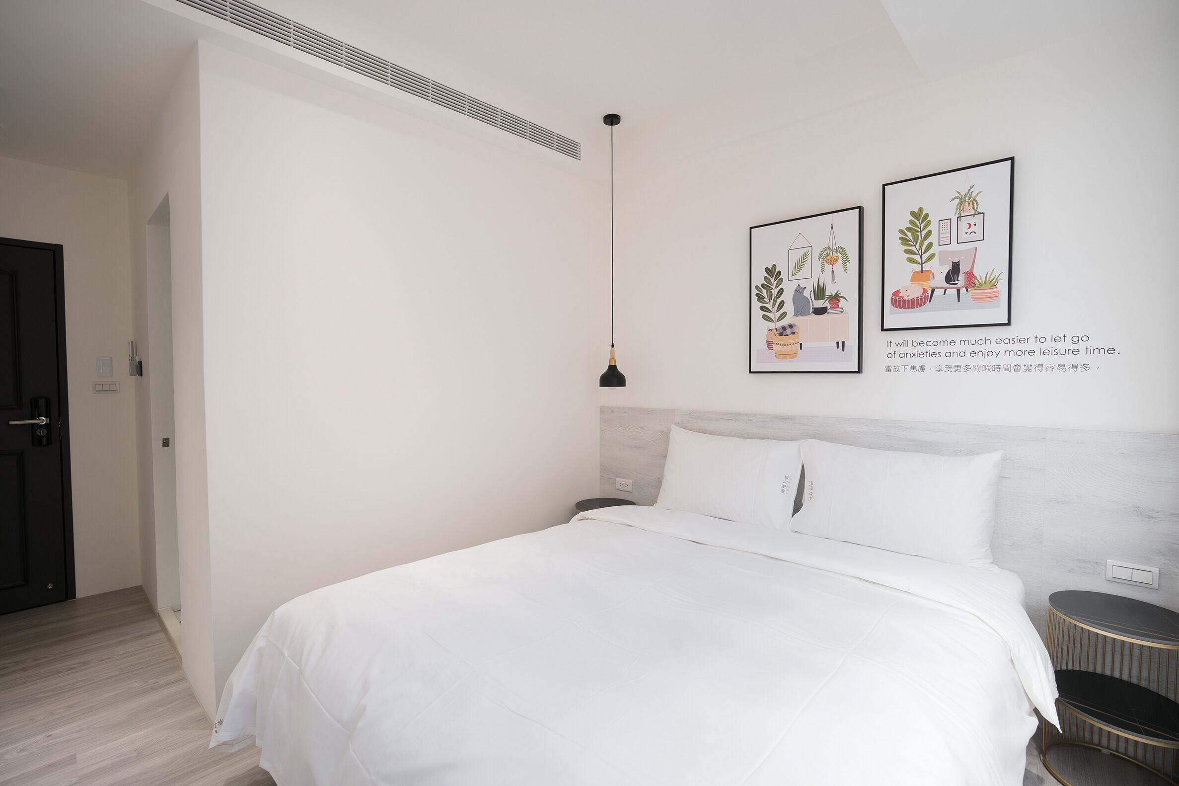 Een moderne slaapkamer met een groot bed, een nachtkastje, een hanglamp en twee ingelijste foto's aan de muur.