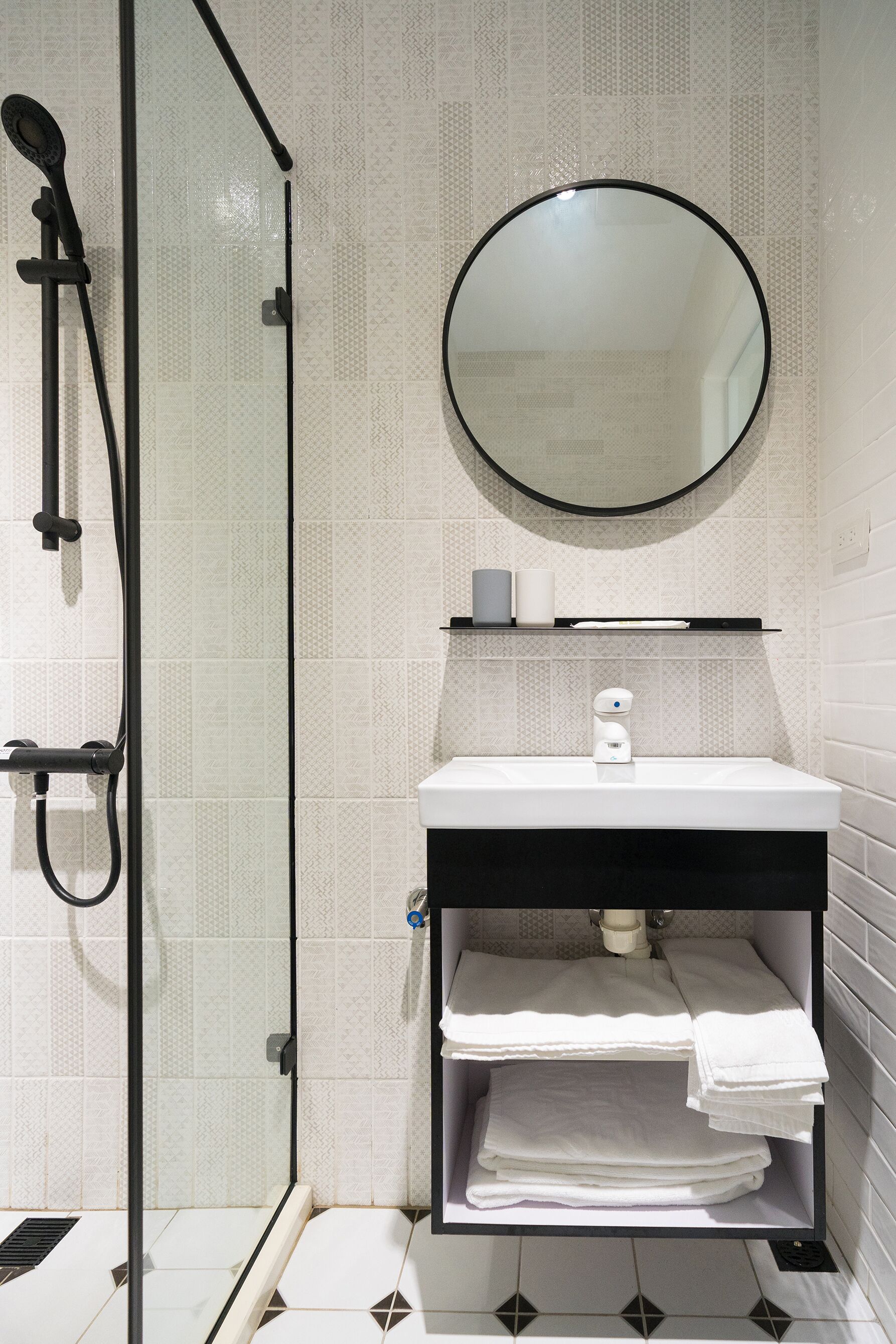 A modern bathroom with a glass shower enclosure, a white sink with a black countertop, and a round mirror above the sink.