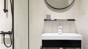 A modern bathroom with a glass shower enclosure, a white sink with a black countertop, and a round mirror above the sink.
