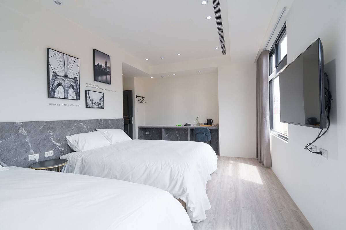 A modern hotel room with two beds, a desk, and a TV.