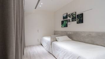 Camera d'hotel moderna con due letti singoli, una testiera grigia e opere d'arte appese al muro.