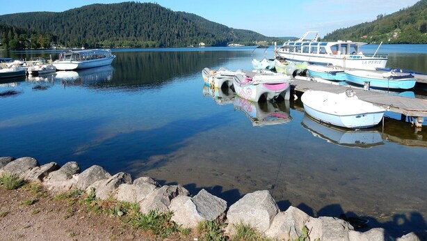 Un lago tranquilo con barcos amarrados en un muelle, rodeado de colinas boscosas.